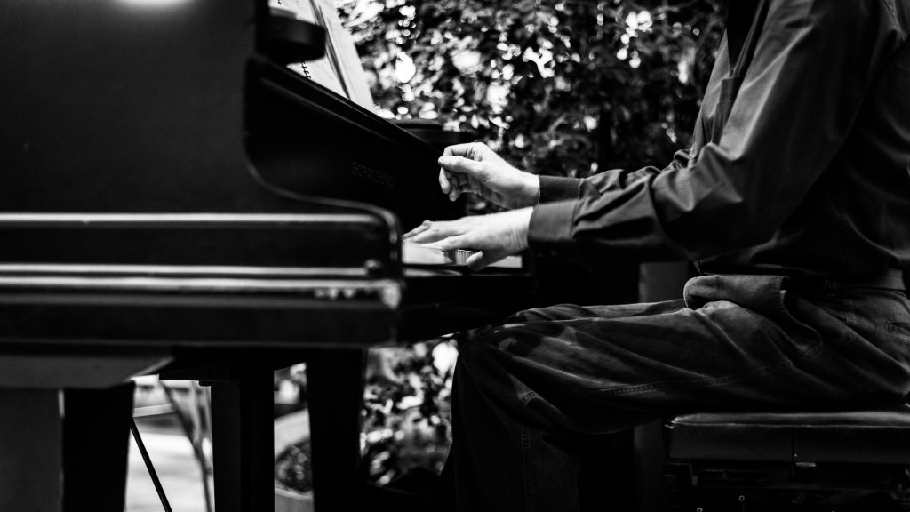 Músico tocando un piano en blanco y negro, con enfoque en sus manos y el teclado, en un entorno exterior.