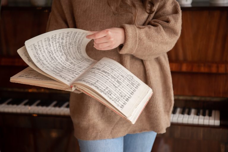 Persona sosteniendo un libro de partituras frente a un piano