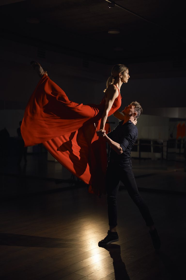Pareja de bailarines realizando una figura con vestido rojo en escena
