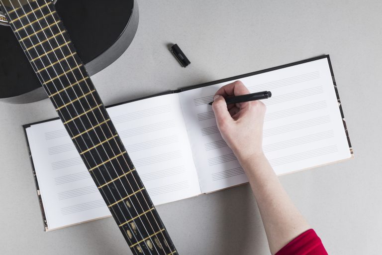 Persona escribiendo partituras junto a una guitarra